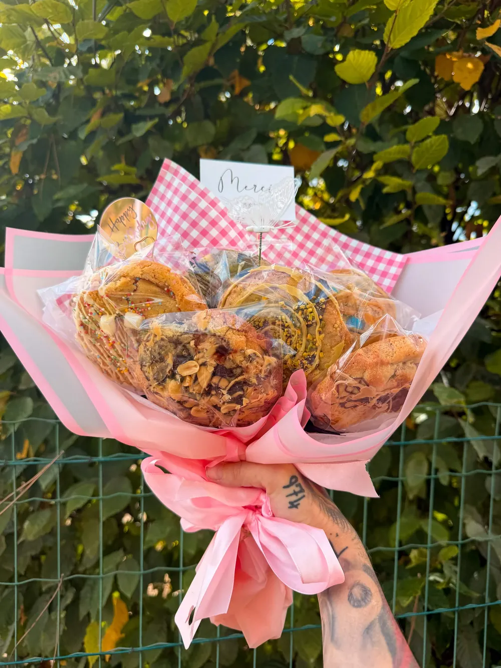 Le bouquet de cookies Chez Mimi tenu à la main : cookies emballés un par un, papier vichy rose, ruban satin, petit mot Merci et papillon